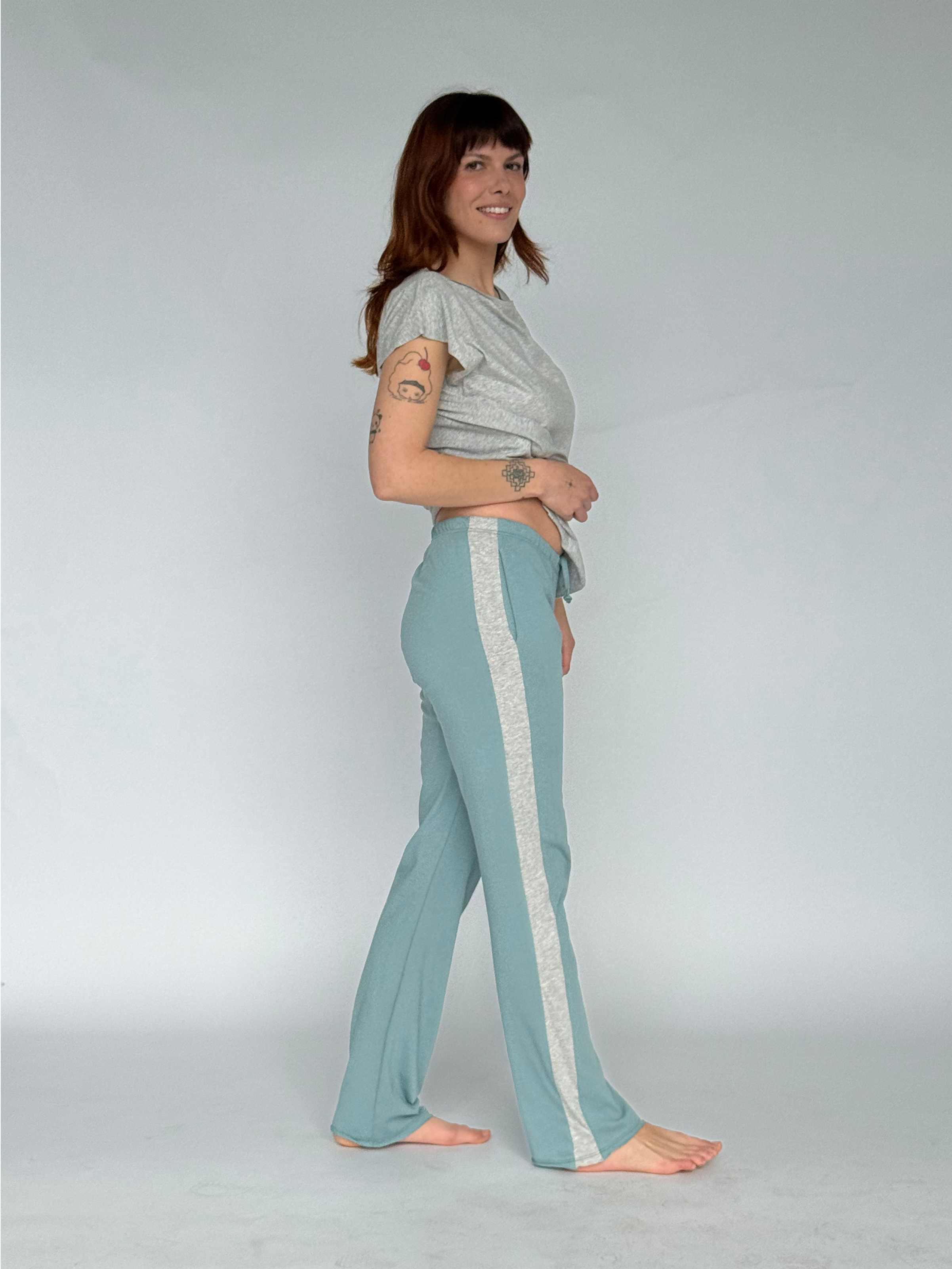 Woman wearing a light gray top and teal pants with white stripes on a plain background