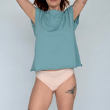 Woman wearing a teal sleeveless top and light pink underwear against a plain background