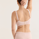 Woman wearing a light pink bra and underwear set on a plain background