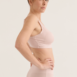 Woman wearing a light pink bra and high-waisted underwear set on a plain background